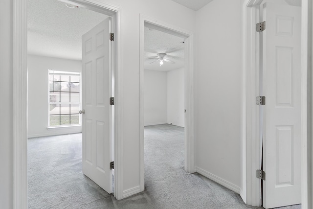 corridor with light carpet and a textured ceiling