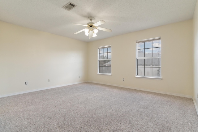 spare room featuring a textured ceiling, light carpet, visible vents, baseboards, and a ceiling fan