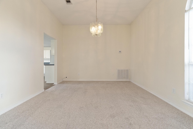 carpeted empty room featuring baseboards, visible vents, and a notable chandelier