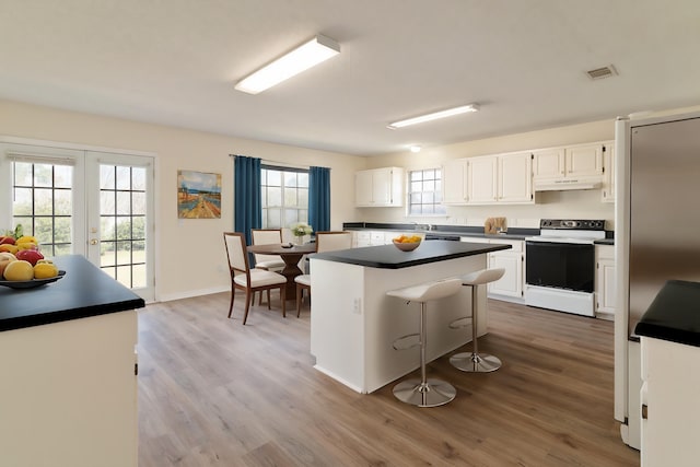 kitchen with visible vents, electric range oven, dark countertops, stainless steel refrigerator, and a center island