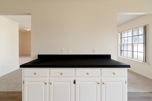 kitchen featuring dark countertops, white cabinetry, baseboards, and light carpet