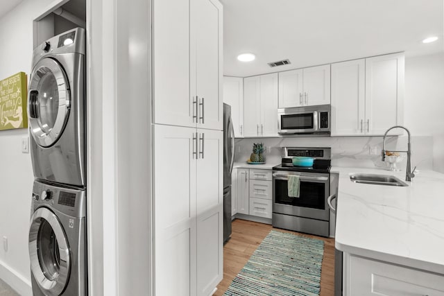 kitchen with stainless steel appliances, light wood-type flooring, stacked washer / drying machine, white cabinets, and sink