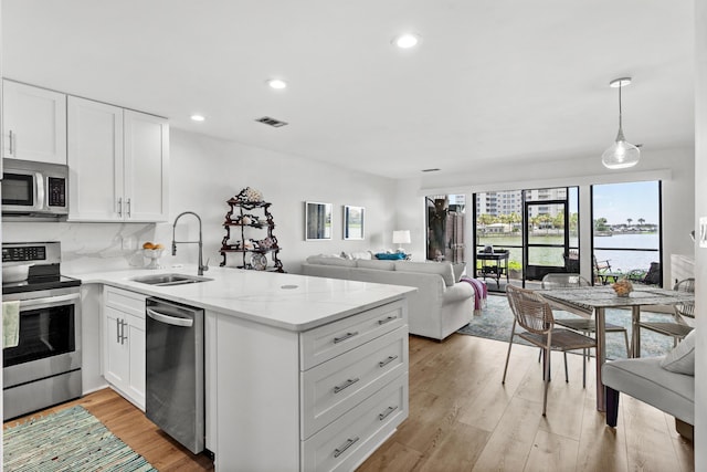 kitchen featuring appliances with stainless steel finishes, light wood-type flooring, sink, white cabinetry, and decorative light fixtures