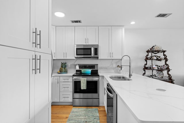 kitchen with sink, white cabinetry, light stone counters, light wood-type flooring, and appliances with stainless steel finishes