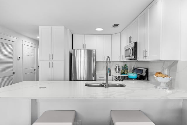 kitchen with kitchen peninsula, a breakfast bar area, white cabinets, appliances with stainless steel finishes, and sink