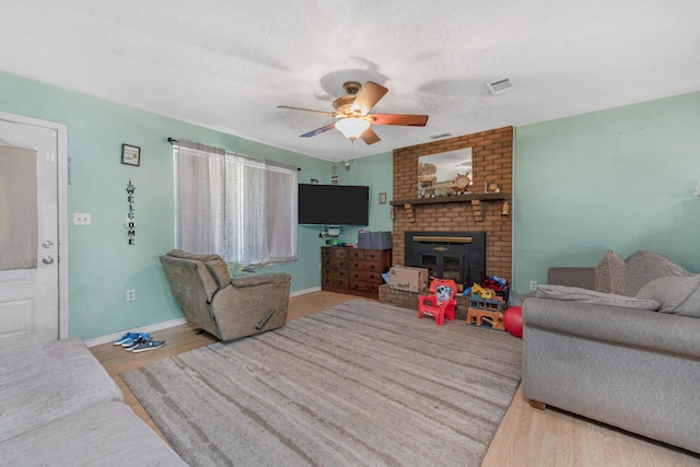 living room featuring light wood-type flooring, ceiling fan, a brick fireplace, and a textured ceiling