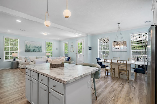 kitchen featuring a center island, light hardwood / wood-style flooring, decorative light fixtures, light stone countertops, and stainless steel fridge