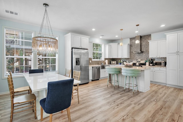 kitchen with appliances with stainless steel finishes, a center island, decorative light fixtures, wall chimney range hood, and white cabinets