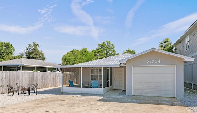 view of front facade featuring fence, concrete driveway, metal roof, a garage, and a sunroom