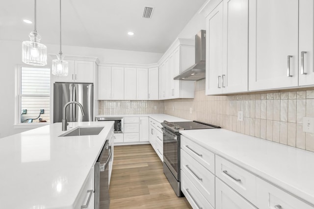 kitchen with wall chimney range hood, decorative light fixtures, light hardwood / wood-style floors, white cabinetry, and stainless steel appliances