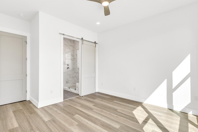 unfurnished bedroom featuring ceiling fan, a barn door, connected bathroom, and light hardwood / wood-style flooring