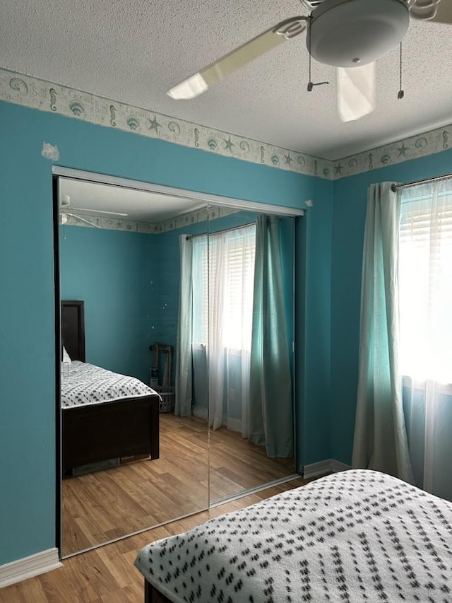 bedroom with hardwood / wood-style flooring, ceiling fan, multiple windows, and a textured ceiling