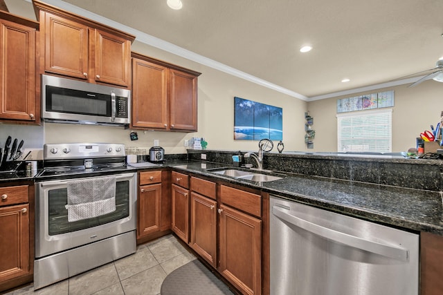 kitchen with sink, light tile patterned floors, appliances with stainless steel finishes, dark stone countertops, and ornamental molding