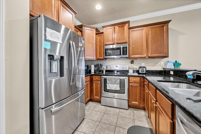 kitchen with light tile patterned floors, sink, appliances with stainless steel finishes, dark stone countertops, and ornamental molding