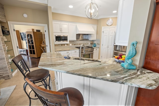 kitchen with appliances with stainless steel finishes, white cabinetry, sink, a breakfast bar, and custom range hood