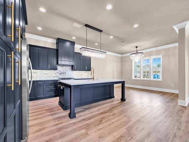 kitchen featuring decorative backsplash, an island with sink, ornamental molding, light hardwood / wood-style floors, and extractor fan