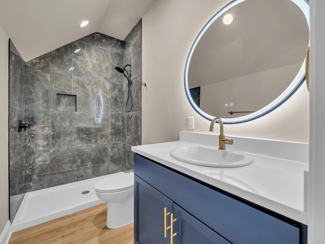 bathroom featuring lofted ceiling, tiled shower, toilet, wood-type flooring, and vanity