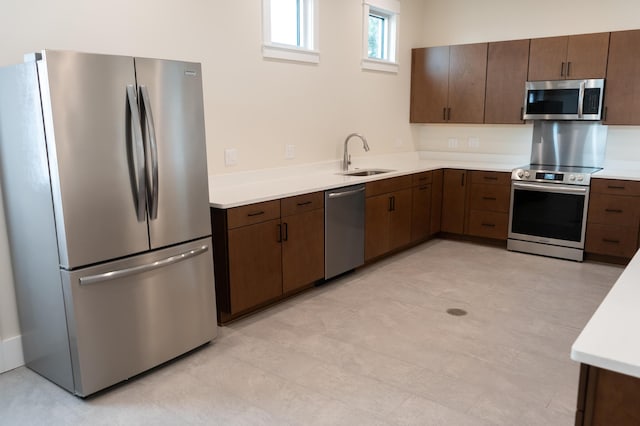 kitchen featuring appliances with stainless steel finishes, light countertops, a sink, and dark brown cabinetry