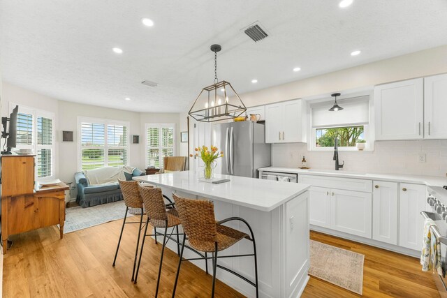 kitchen featuring stainless steel appliances, light hardwood / wood-style floors, a kitchen island, decorative backsplash, and white cabinetry