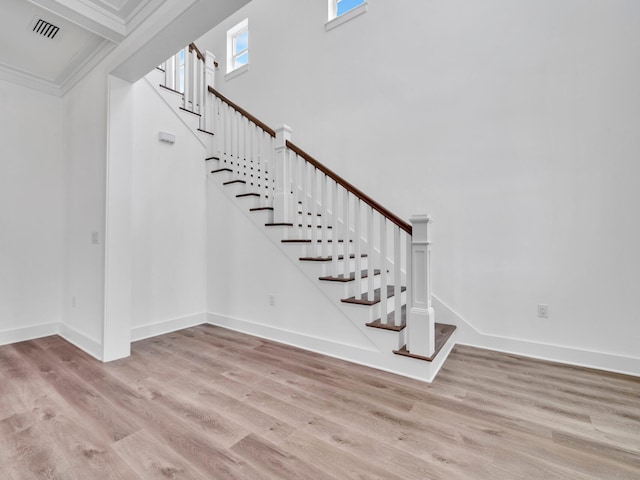 staircase featuring light hardwood / wood-style floors, crown molding, and a towering ceiling