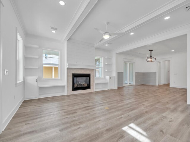 unfurnished living room featuring ceiling fan, built in shelves, beam ceiling, light hardwood / wood-style flooring, and a tiled fireplace