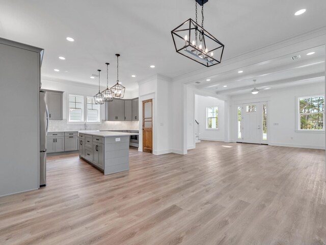 kitchen with crown molding, light hardwood / wood-style flooring, backsplash, a center island, and gray cabinets