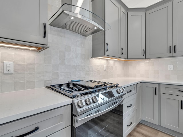 kitchen with wall chimney range hood, decorative backsplash, light wood-type flooring, and stainless steel gas stove