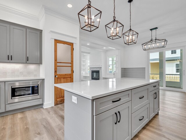 kitchen with light hardwood / wood-style floors, stainless steel microwave, tasteful backsplash, and crown molding