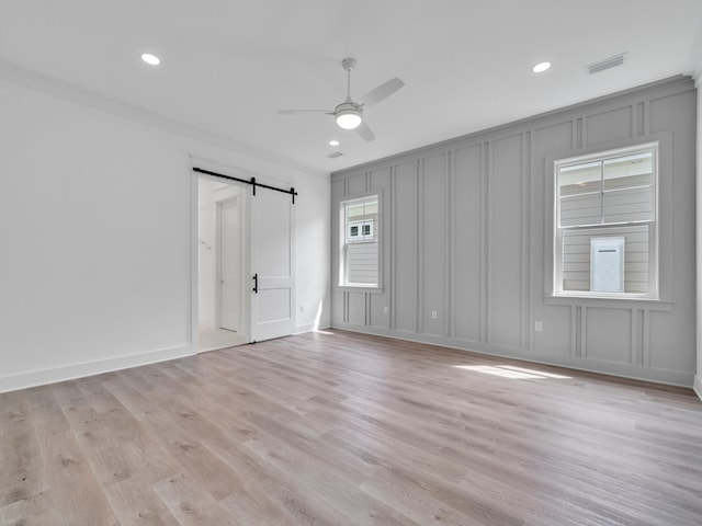 unfurnished room with light hardwood / wood-style floors, crown molding, and a barn door