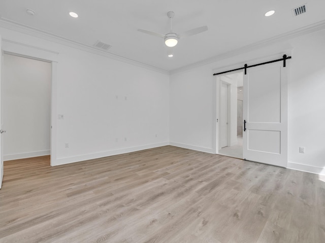 empty room with light hardwood / wood-style flooring, ornamental molding, a barn door, and ceiling fan