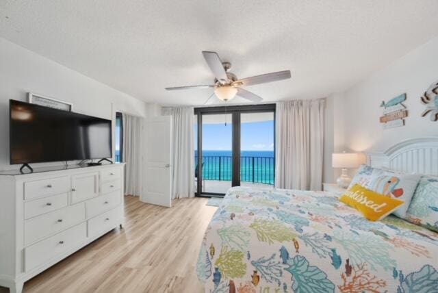 bedroom featuring a water view, access to exterior, ceiling fan, light hardwood / wood-style floors, and expansive windows