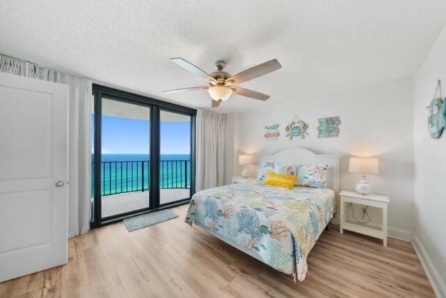 bedroom featuring light wood-type flooring, a water view, access to exterior, ceiling fan, and expansive windows