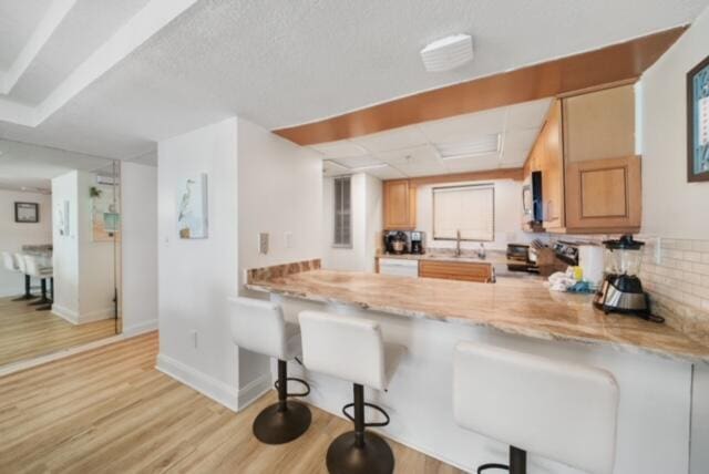 kitchen featuring a breakfast bar, light hardwood / wood-style flooring, kitchen peninsula, backsplash, and sink