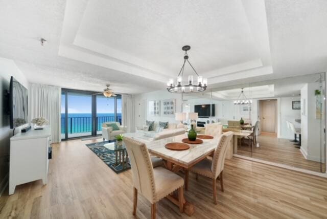 dining room featuring ceiling fan with notable chandelier, light hardwood / wood-style floors, a water view, and a tray ceiling