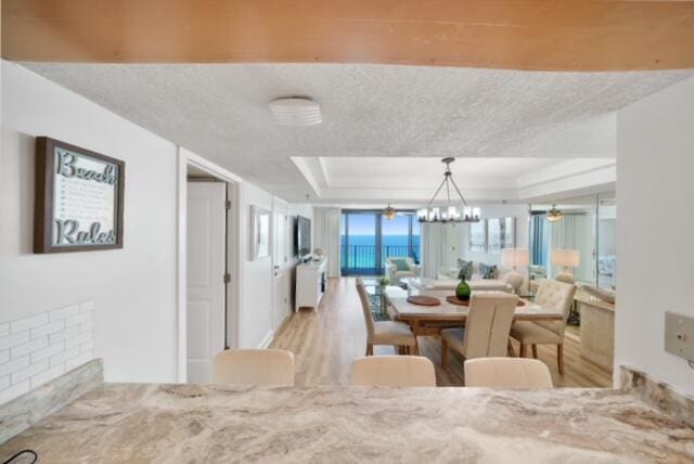 dining area with a textured ceiling, ceiling fan with notable chandelier, a raised ceiling, and light hardwood / wood-style floors