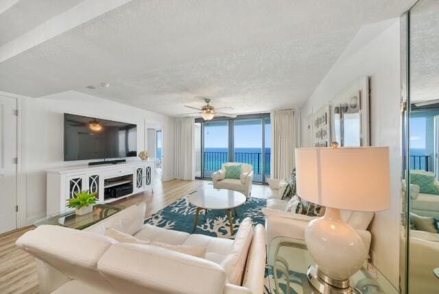 living room featuring light hardwood / wood-style flooring, a water view, expansive windows, a textured ceiling, and ceiling fan