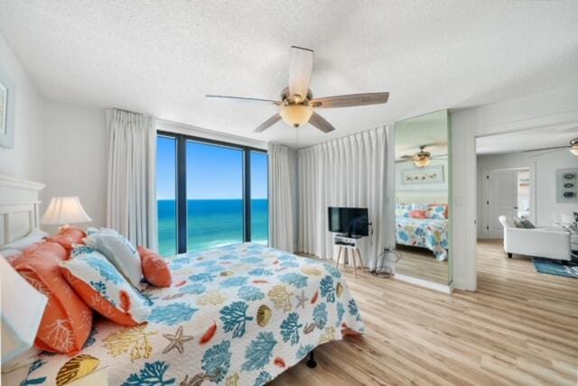 bedroom featuring access to exterior, a water view, light wood-type flooring, a textured ceiling, and ceiling fan