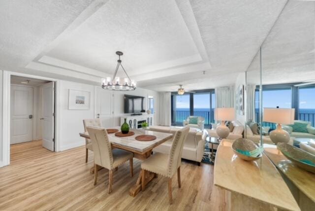 dining area with a textured ceiling, ceiling fan with notable chandelier, light wood-type flooring, and a tray ceiling