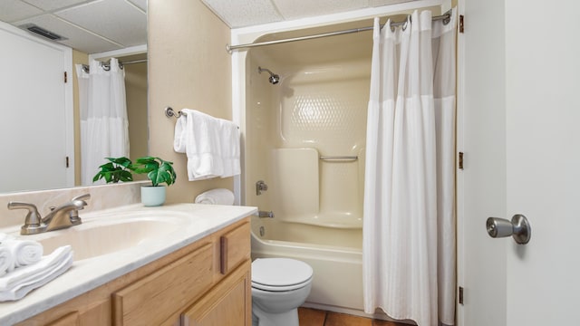 full bathroom with shower / tub combo, tile patterned flooring, a drop ceiling, toilet, and vanity