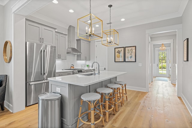 kitchen with stainless steel appliances, wall chimney range hood, decorative light fixtures, a breakfast bar area, and a center island with sink