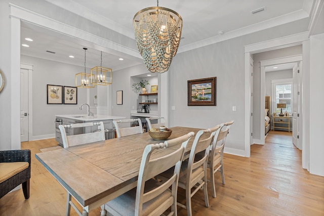 dining room featuring light hardwood / wood-style floors, sink, ornamental molding, and a notable chandelier