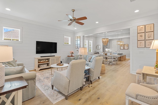 living room featuring wood walls, light hardwood / wood-style flooring, ceiling fan with notable chandelier, and ornamental molding