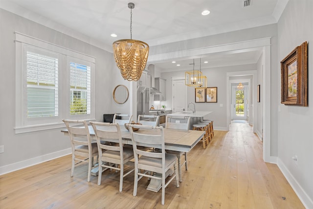 dining space featuring crown molding, sink, light hardwood / wood-style floors, and an inviting chandelier