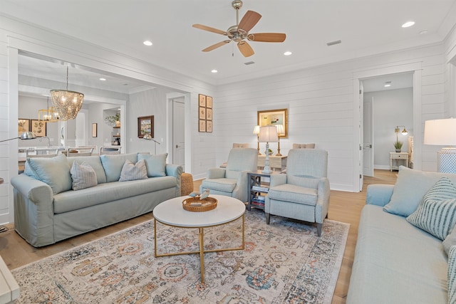 living room with ceiling fan with notable chandelier, light wood-type flooring, and crown molding