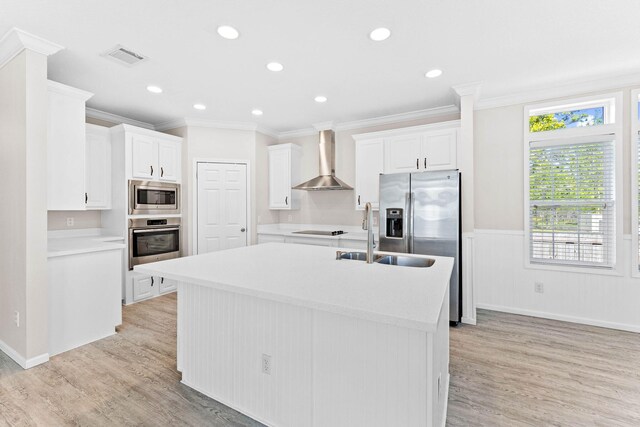 kitchen featuring appliances with stainless steel finishes, an island with sink, sink, white cabinets, and wall chimney exhaust hood