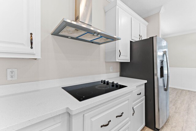 kitchen featuring wall chimney range hood, crown molding, white cabinets, black electric cooktop, and light wood-type flooring