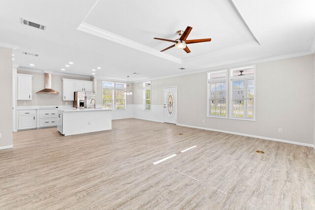 unfurnished living room with a raised ceiling, ornamental molding, ceiling fan, and light wood-type flooring