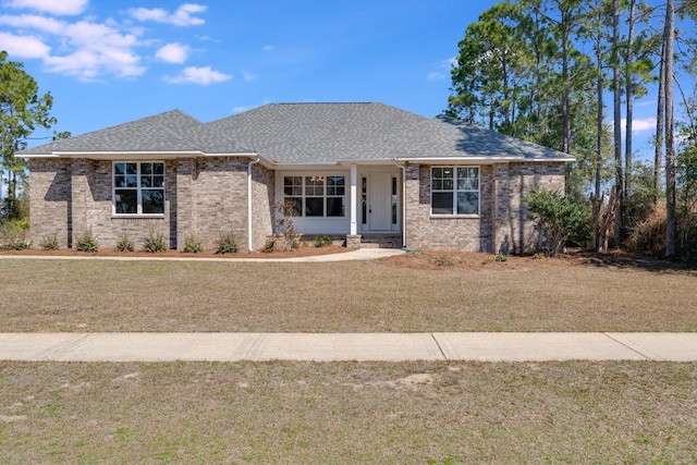 view of front of property featuring brick siding, roof with shingles, and a front yard