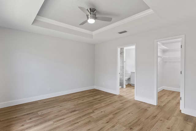 unfurnished bedroom with crown molding, a spacious closet, a raised ceiling, and light wood-type flooring