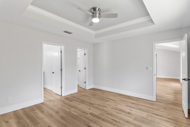 unfurnished bedroom with a spacious closet, ornamental molding, a tray ceiling, ceiling fan, and light hardwood / wood-style floors